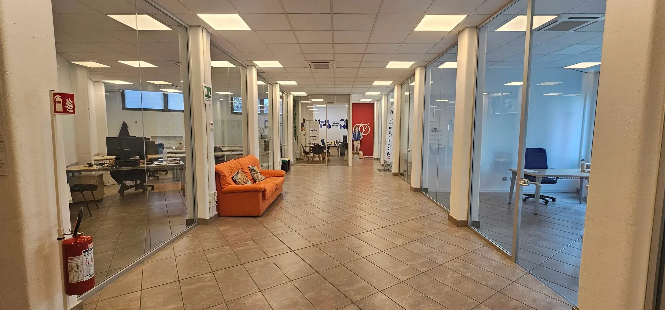 The private-office corridor at Fabbriche Binarie, with the glass walls and the orange sofa